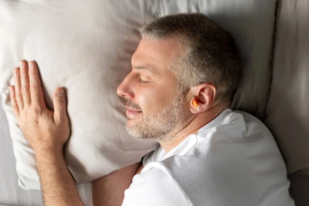 Middle aged man sleeping on his side with earplugs in his ears