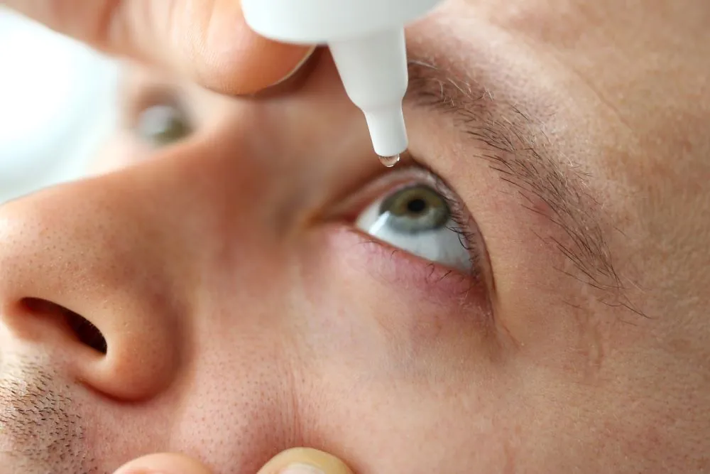 Man putting eye drops in his eyes